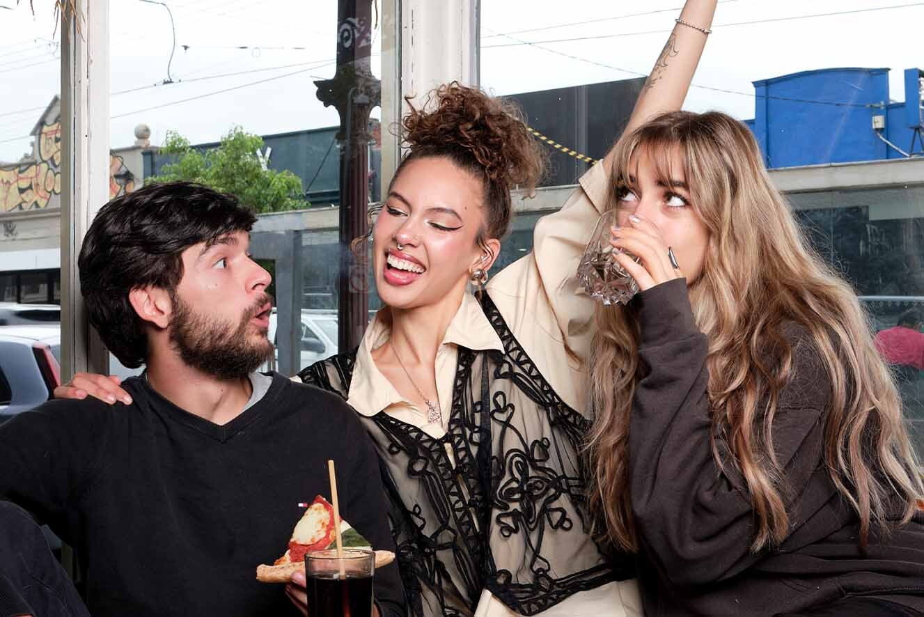 Three friends, a young man and two young women, sit in a café eating pizza. Three friends, a young man and two young women, sit in a café eating pizza.