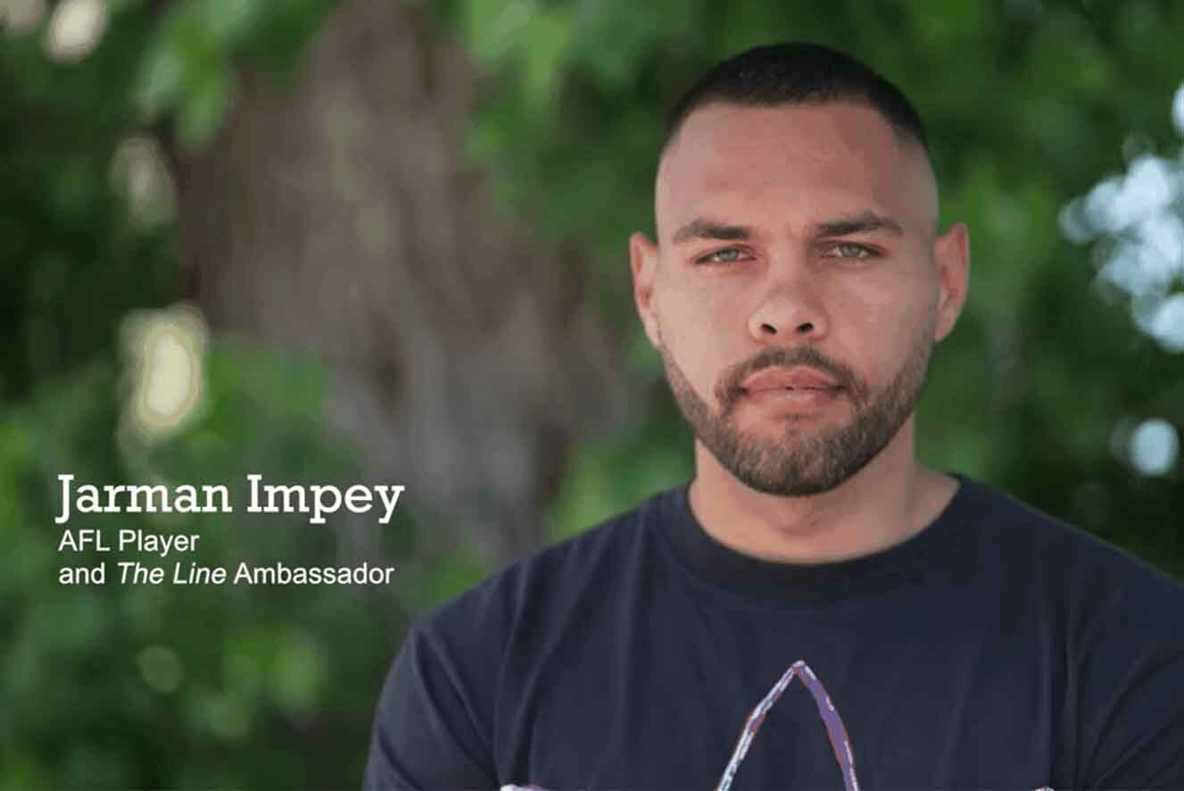 Hawthorn Aboriginal AFL player Jarman Impey stands in front of a tree with green leaves. He has stubble on his face and is wearing a black t-shirt. In the bottom-left corner of the image are the words: "JARMAN IMPEY, AFL Player and The Line Ambassador".