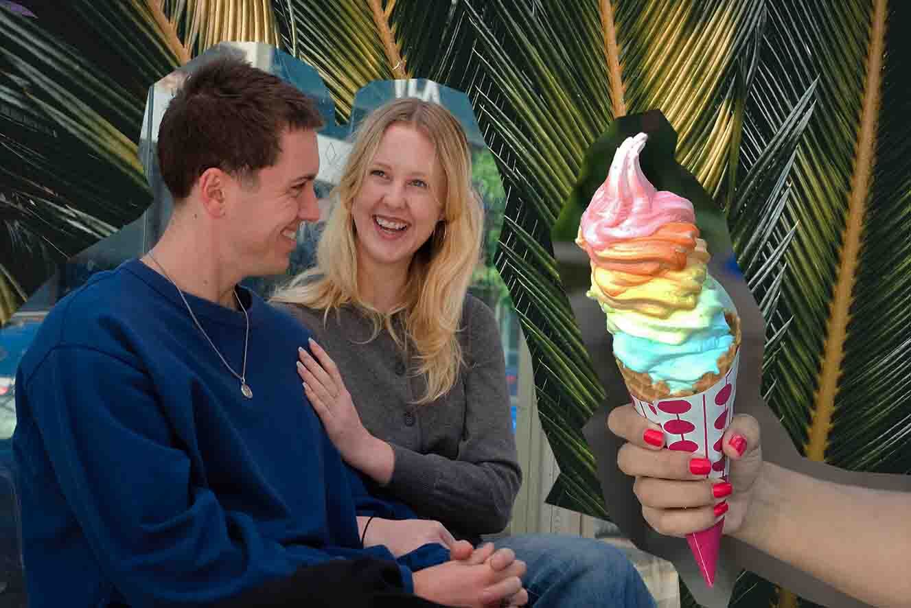 A young women and man  sitting in front of tropical palm leaves, smiling. To their left a hand holds a colourful soft serve ice cream cone.