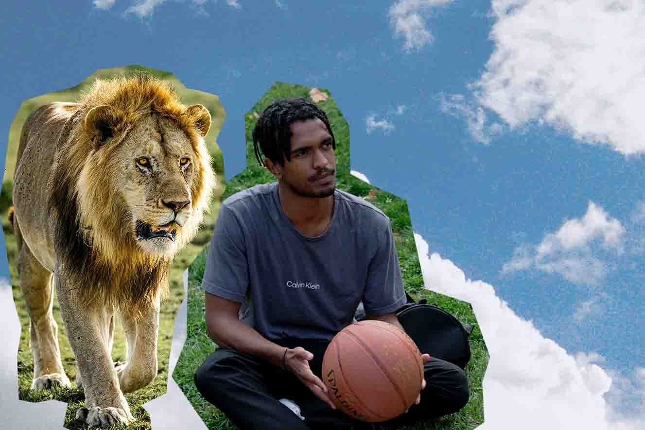 A young male with dark skin sitting with a basketball next to a lion against a backdrop of clouds.