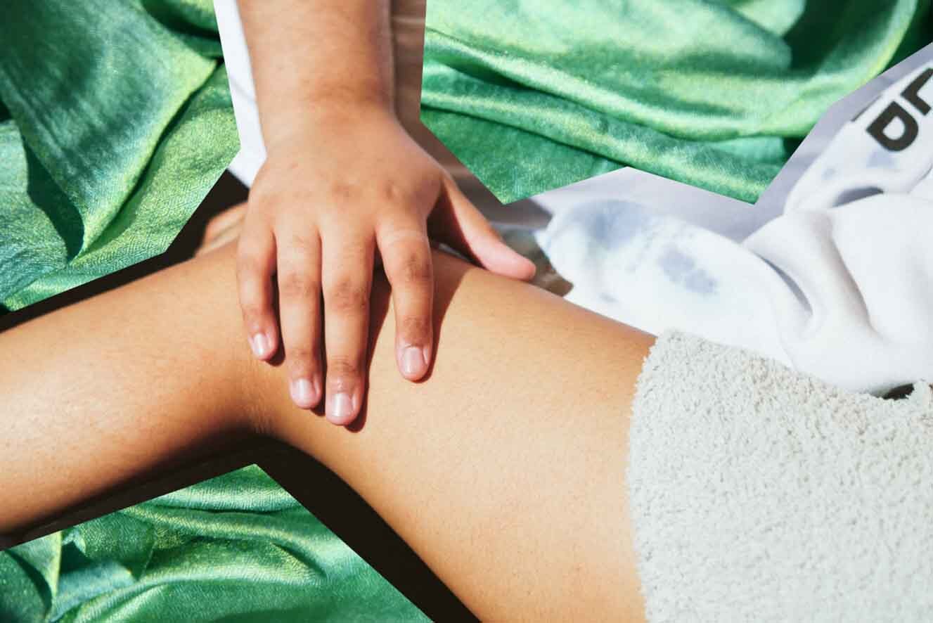 Close-up of a hand resting on a bare leg against a green fabric background.