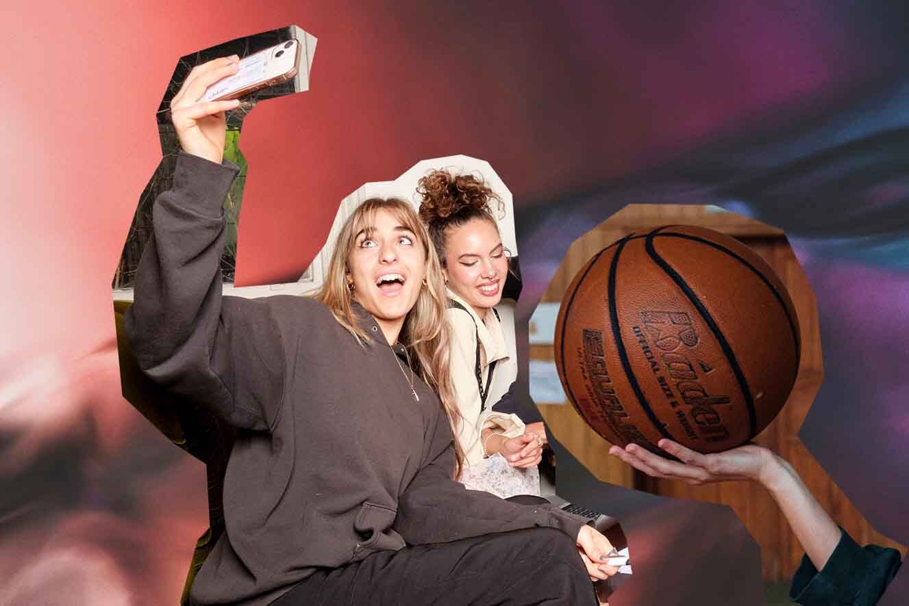 Two people having fun with one holding a smartphone and taking a selfie, another hand offering a basketball to them, against a dynamic pink and red backdrop.