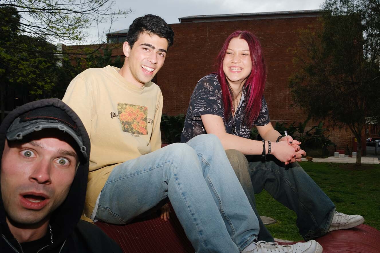 Three young people on a bench outside. Three young people on a bench outside.