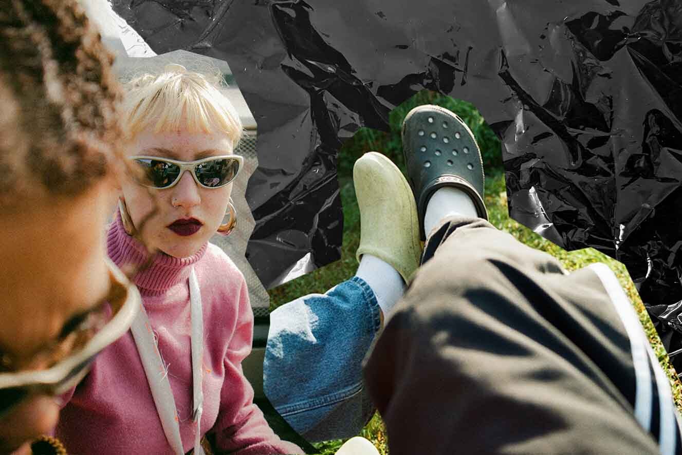 Two people wearing sunglasses are sitting outside, one with blonde hair visible, the other partially shown with curly hair. They wear colorful outfits. To their left is two legs touching wearing green and white crocs. The background is artistically crumpled with a monochrome effect.