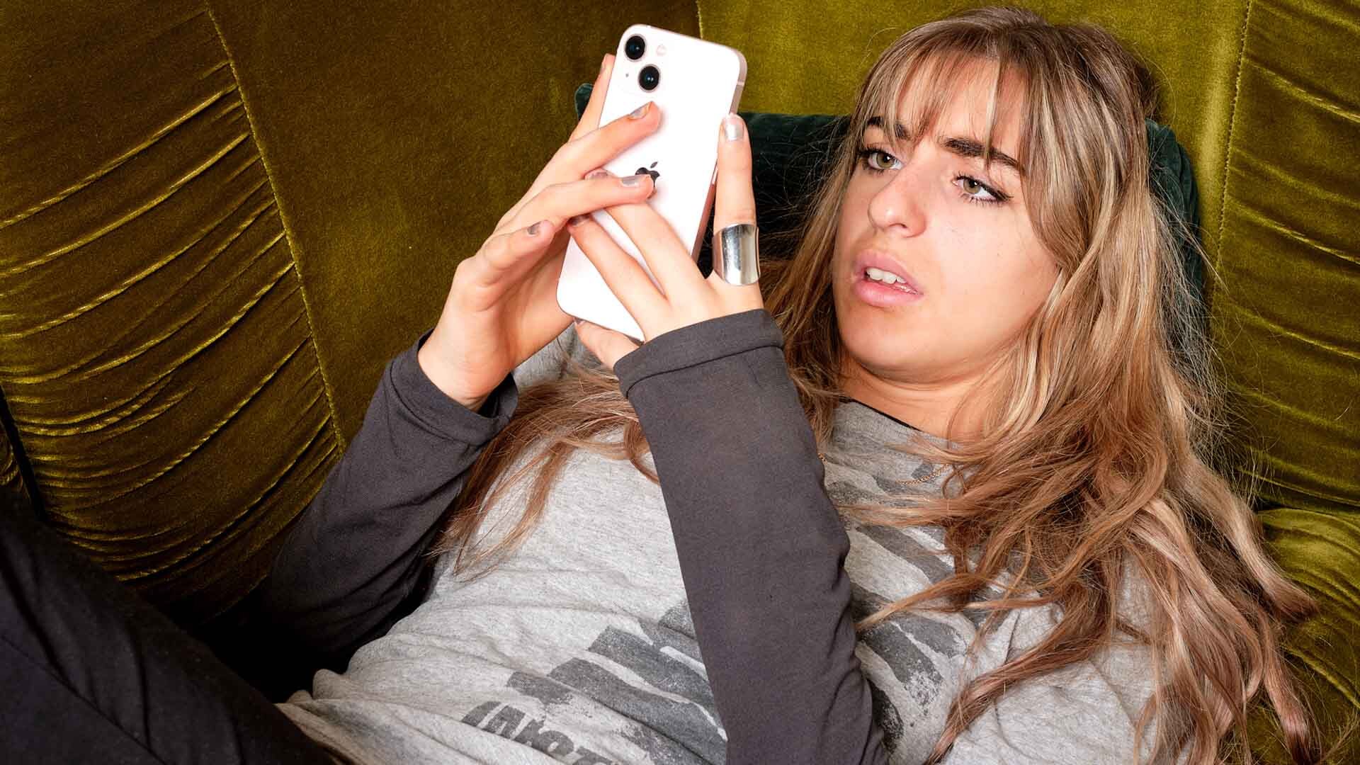 A young woman looks concerningly at her phone. A young woman looks concerningly at her phone.