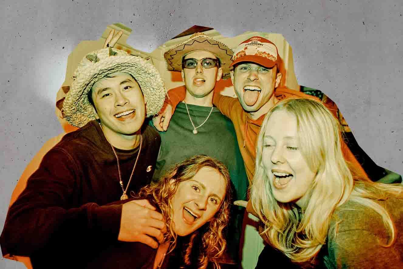 Group of five people smiling and posing closely together, dressed in casual, colorful attire.