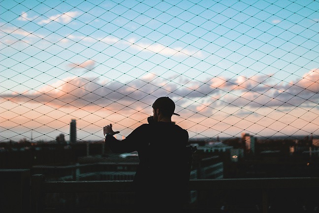 Man standing behind chain link fence looking out over a cityscape