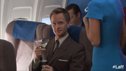 GIF of actor Neil Patrick Harris on a plane, about to sip a martini and looking smug